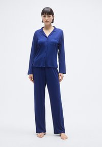 Σετ πυτζάμας σε ναυτικό μπλε χρώμα με επάνω μέρος με κουμπιά και μακριά μανίκια, τσέπη στο στήθος και παντελόνι με άνετη εφαρμογή και μαλακή υφή.