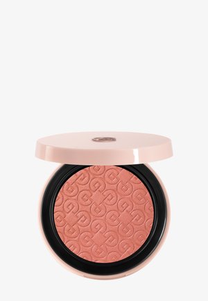 Blush compact rond avec motif embossé dans une teinte rose poudré, logé dans un étui rose clair avec un couvercle partiellement ouvert sur fond blanc.