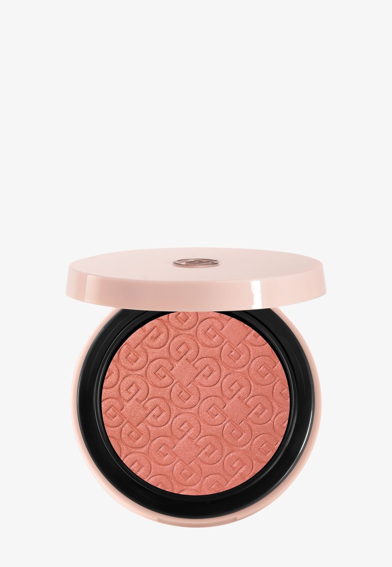 Blush compact rond avec motif embossé dans une teinte rose poudré, logé dans un étui rose clair avec un couvercle partiellement ouvert sur fond blanc.