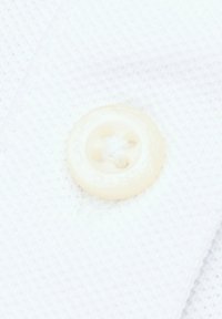 Biała tkanina o teksturowanej powierzchni z kremowym plastikowym guzikiem, umiejscowionym w centralnej części, z lekko wypukłym wzorem i otworami.