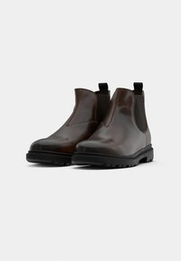 Pair of glossy brown leather Chelsea boots with black elastic side panels and thick black rubber soles on white background.