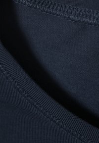 Tissu bleu marine avec une texture lisse et un gros plan sur un décolleté arrondi. Il présente des coutures contrastées le long du bord.