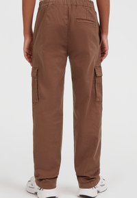 Pantaloni cargo marroni con vita elastica, tasche laterali e una tasca posteriore applicata. Realizzati in tessuto leggero con una superficie liscia.
