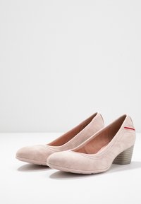 Růžové semišové lodičky s kulatou špičkou, zdobené tónovaným prošíváním a jemným červeným akcentem na zadní straně. Podpatky mají strukturovaný povrch.