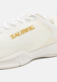Fehér sportcipő texturált felsőrésszel, arany "SALMING" márkázással. A fűzők fehérek, a talp pedig letisztult, kerekdizájnú.