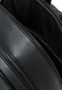 Mochila negra de material sintético mate, con múltiples compartimentos con cremallera y un forro interior estampado con el nombre de la marca.