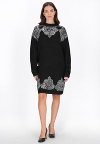 Zwarte gebreide jurk met zilveren sierlijke versieringen op de schouders en de zoom, met lange mouwen en een losse pasvorm.