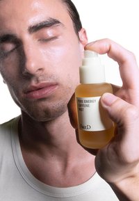 Nebulizzatore di caffeina in una bottiglia di vetro trasparente con un erogatore bianco, spruzzato sul viso di una persona. Bottiglia etichettata "Nebulizzatore di Caffeina Pure Energy".