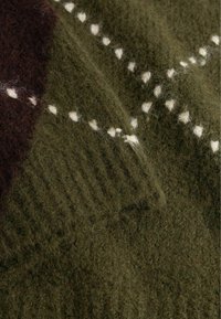 Gros plan d'un tissu tricoté doux et duveteux vert olive avec un motif à pois blancs et une texture côtelée sur un pull plié.