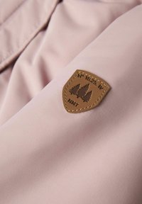 Gaiši rozā audums ar brūnu ādas plati, kurai ir iegravēts koka dizains un ģeogrāfiskās koordinātas, izšūtas gar malām.