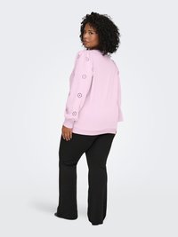 Light pink pullover sweater with eyelet embellishments on sleeves, paired with black flared pants. Soft fabric with a relaxed fit.