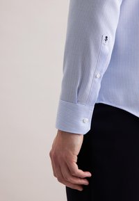 Lichtblauw en wit gestreept shirt met knoopmanchetten. Heeft een subtiele geborduurde accent nabij de manchette. Gladde stofstructuur.