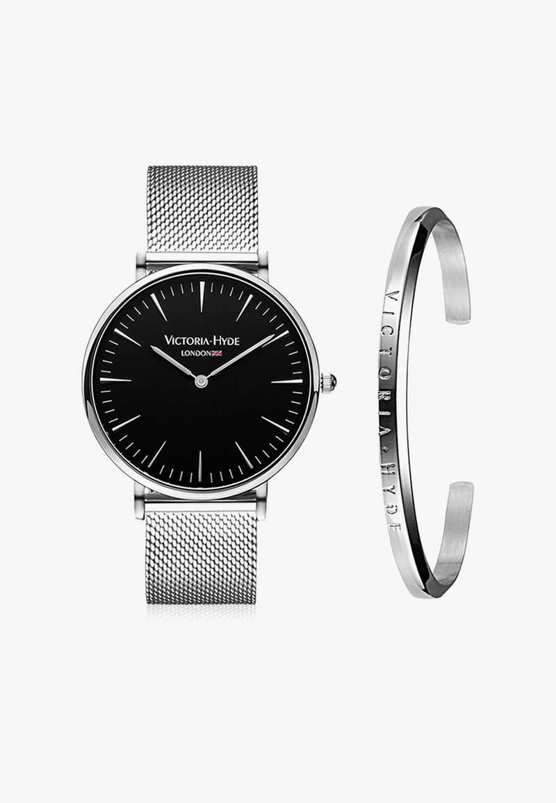 Sort urskive med sølv mesh rem, der har tynde time markører og visere. Leveres med et sølv armbånd med prægede brandnavn.
