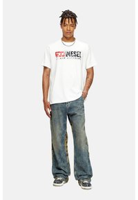 Hvid kortærmet T-shirt med rød og sort grafisk print, et par blå denimjeans med mønstrede sidelapper og casual sneakers.