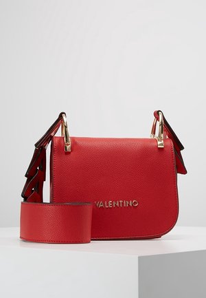 Sac bandoulière en cuir rouge avec ferrures dorées, présentant une finition texturée et des accents uniques en forme d'ailes sur la sangle. Logo de la marque visible.