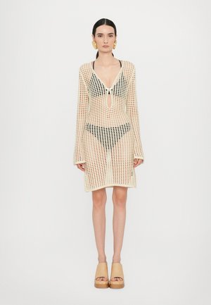 Crochet mesh cover-up dress in cream with long sleeves, deep V-neck, keyhole detail, and a fitted silhouette, paired with black swimwear underneath.