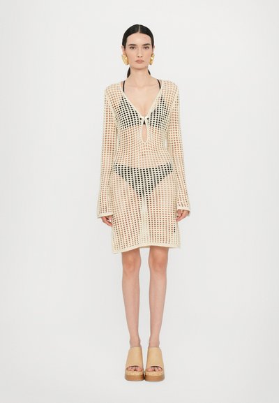 Crochet mesh cover-up dress in cream with long sleeves, deep V-neck, keyhole detail, and a fitted silhouette, paired with black swimwear underneath.