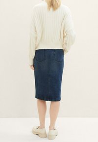 Jersey de punto acanalado en color crema con hombros caídos combinado con una falda midi vaquera en azul oscuro. Se llevan zapatos de plataforma gruesa blancos.