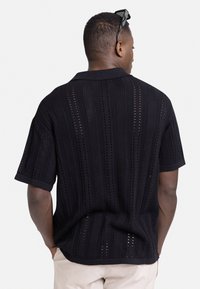 Polo negro de punto de manga corta con rayas verticales, que presenta patrones de tejido abierto. Cuello y dobladillo de canalé, corte relajado y espalda lisa.