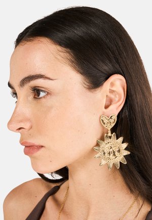 Goldene Tropfohrringe mit einem herzförmigen Stecker und einem Sonnensymbol mit Strahlen. Filigrane, strukturierte Muster im gesamten Metalldesign.