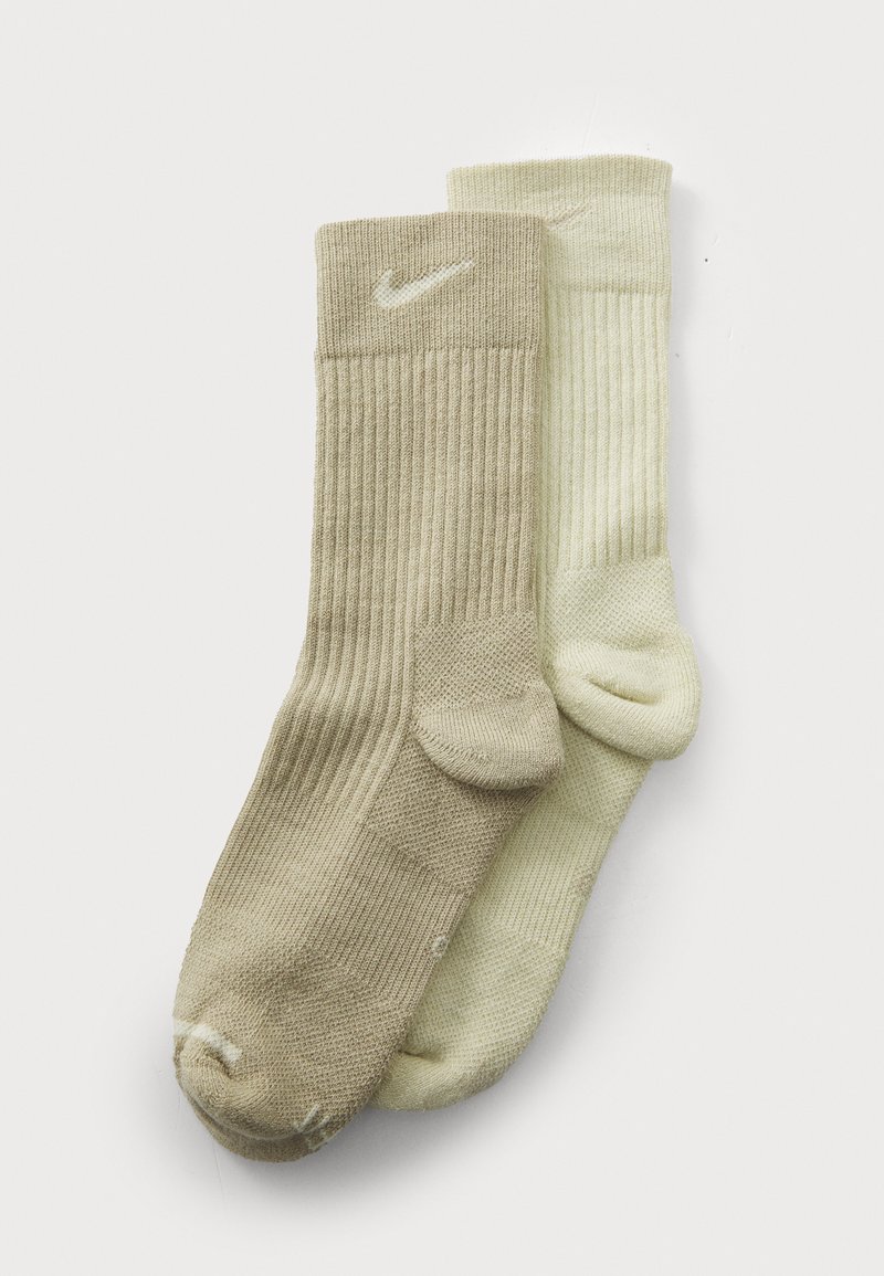 Calcetines tobilleros en color beige y verde claro, con textura acanalada, que presentan un pequeño logo blanco en el puño, con refuerzos en la zona del talón y los dedos.