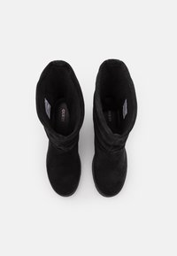 Černé kotníkové boty z semiše s volným designem, měkkou texturou a zaoblenou špičkou. Vnitřek zdobí značka. Jednoduchý, minimalistický vzhled.
