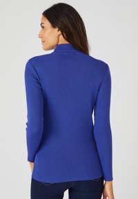 Maglione a collo alto a coste in blu vivace, design aderente, maniche lunghe, si estende fino ai fianchi, caratterizzato da una texture liscia e un collo alto.
