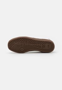 Brown rubber shoe sole with a textured pattern featuring hexagonal grips and a circular detail. The edge is slightly raised around the perimeter.
