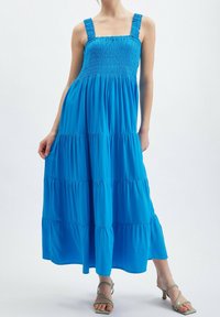 Blå maxi-klänning med smockad byst och justerbara axelband. Har flerskiktade volanger och en feminin silhuett. Slät tyg och livfull färg.