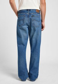 Jeans de mezclilla azul con corte recto, cinco bolsillos, costuras amarillas y una etiqueta de cuero en la parte posterior de la cintura. Textura suave, diseño casual.