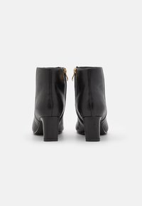 Botas de tobillo de cuero negro con una textura suave, punta redondeada, tacón bloque de altura media y cremalleras laterales doradas para el cierre.