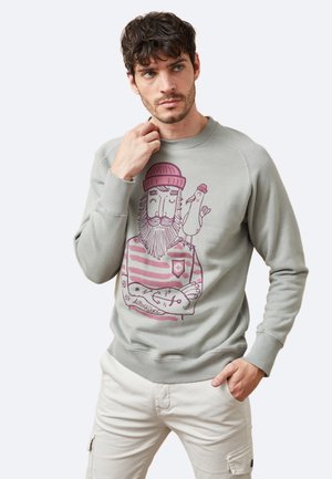 Sudadera gris claro con cuello redondo acanalado, que presenta una impresión de un hombre con barba vestido con una camiseta a rayas y un sombrero de lana rosa.