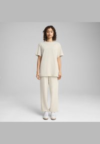 Beige oversized T-shirt med korte ærmer, der har et lille broderet logo. Sættes sammen med beige vide bukser og hvide sneakers.