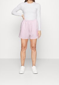Pantaloncini di cotone rosa chiaro con vita elastica, caratterizzati da una vestibilità comoda. Abbinati a una maglia grigia a maniche lunghe e sneakers bianche.