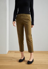 Kaki cropped byxor med rak ben, fickdetaljer och en jämn textur, kombinerat med svarta lägenheter och en åtsittande svart tröja.