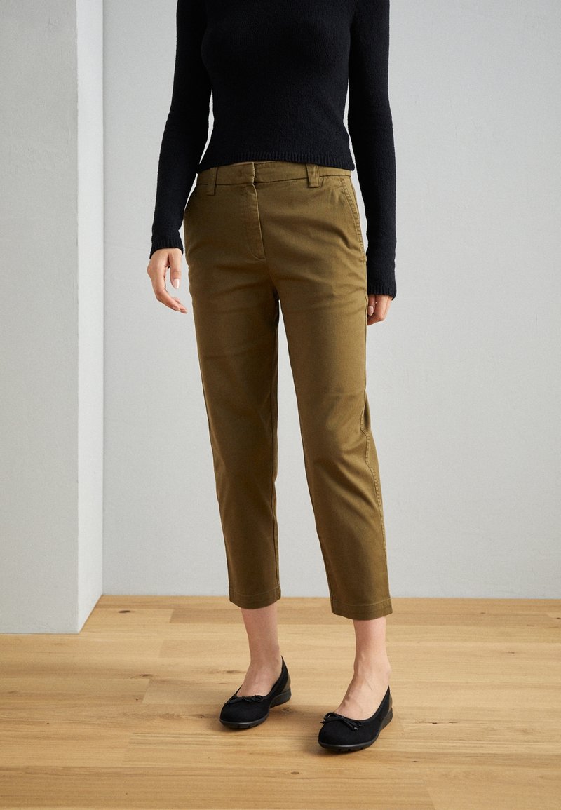 Kaki cropped byxor med rak ben, fickdetaljer och en jämn textur, kombinerat med svarta lägenheter och en åtsittande svart tröja.