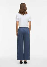 Blauwe wijde broek met een elastische tailleband, gedragen met een wit shirt met korte mouwen. De outfit heeft een relaxte pasvorm en een zachte textuur.