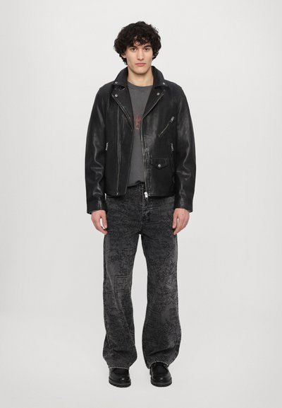 Jachetă de motociclist din piele neagră cu accente de fermoar, tricou gri cu grafică și blugi negri largi cu modele texturate. Botine negre.