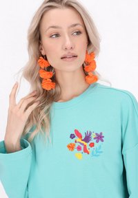 Felpa turchese con una vestibilità comoda e maniche lunghe, caratterizzata da vivaci ricami di un pappagallo e fiori sul davanti.