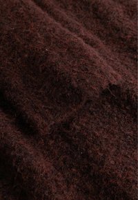 Nærbilde av mørkebrunt, teksturert ullstoff med synlige myke fibre og krøllete trådmønstre.