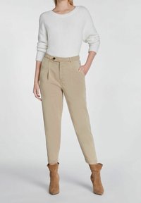 Pantalones plisados beige con bolsillos laterales, combinados con un suéter de punto blanco y botas de tobillo marrones. Textura suave y diseño ajustado.