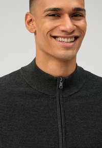 Donkergrijze sweater met rits en een geribbeld textuur en hoge kraag. Voorzien van een rits aan de voorkant en een aansluitend ontwerp.