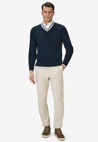 Mörkblå tröja med V-hals och vit randig krage, tillsammans med beiga byxor och bruna snörskor.