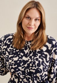 Chemise boutonnée en motif abstrait bleu marine et crème, avec une coupe décontractée, un col rond et des manches courtes à texture subtile.