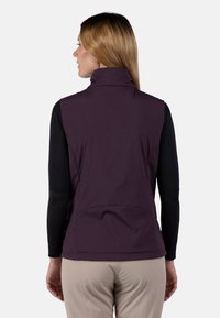 Violette ärmellose Weste mit hohem Kragen, Rückennahtdetails und einer leichten, glatten Struktur; getragen über einem schwarzen Langarmshirt.