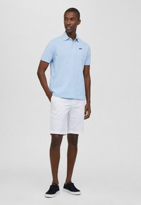 Jasnoniebieska koszulka polo z kieszonką, w połączeniu z białymi szortami i ciemnymi sneakersami. Gładka faktura, klasyczny krój kołnierzyka, luźny fason.