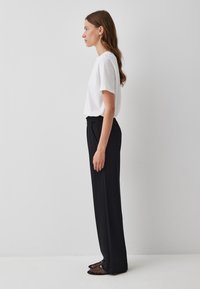 Witte korte mouwen t-shirt gecombineerd met hoge zwarte broek. De broek heeft een gladde textuur en een elastische tailleband. Zwarte mesh instappers maken de look compleet.
