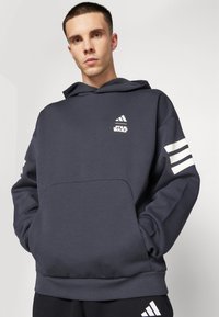 Temno moder hooded pulover z vorno žepom, belimi detajli s tremi črtami na rokavih ter logotipoma Adidas in Star Wars.