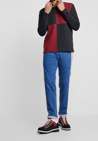 Långärmad polo, svart och vinröd färgblock, bomullsblandning. Blå jeans med beigefärgade sidopaneler. Svarta stövlar med röda snören och gyllene öglor.