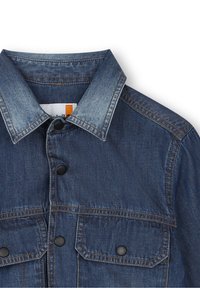 Džínová bunda s tmavě modrým odstínem, s špičatým límcem, dvěma předními kapsami se černými patentkami a kontrastními švy.